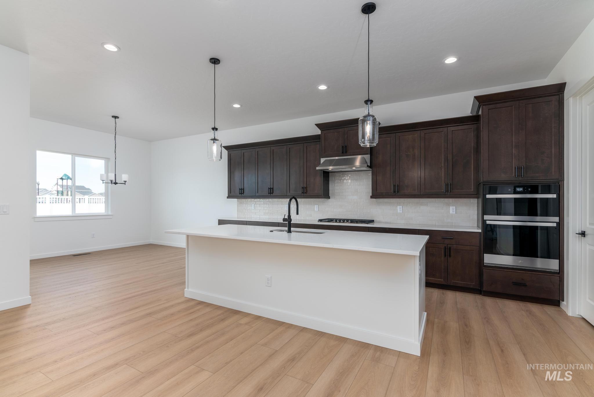 8459 South Country Wind Avenue Meridian, ID 83642 - Photo 6 of 11 Kitchen featuring dark wood finish cabinets, double oven, an island with sink, and suspended lighting