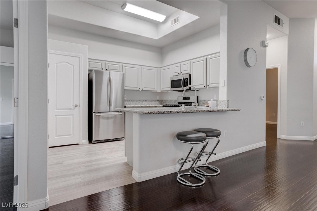 2305 West Horizon Ridge Parkway, Unit 3921 Henderson, NV 89052 - Photo 19 of 31 Kitchen featuring appliances with stainless steel finishes, a peninsula, light wood-type flooring, white cabinetry, and light stone counters