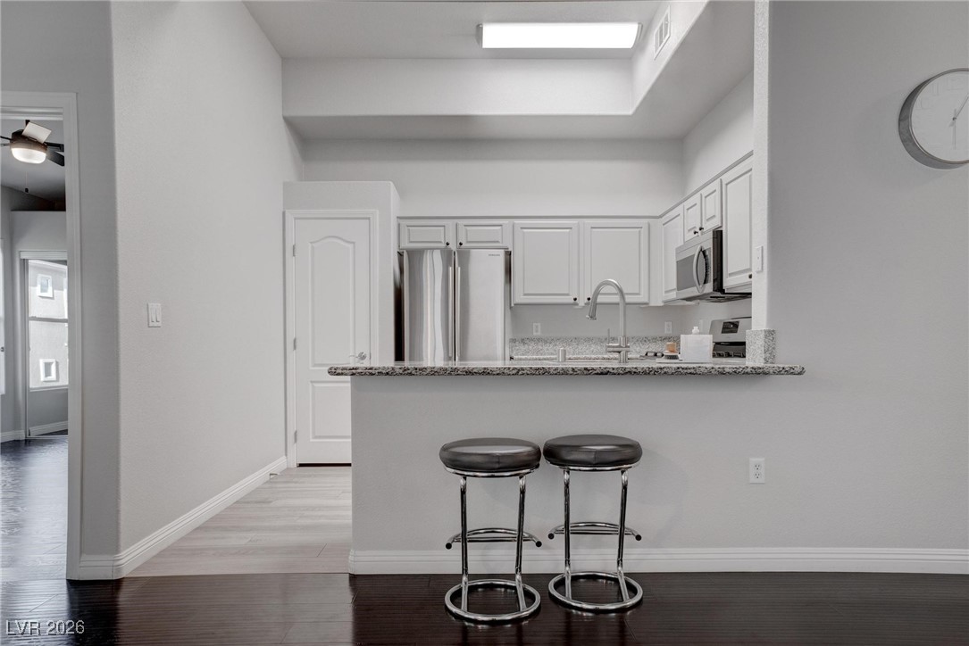 2305 West Horizon Ridge Parkway, Unit 3921 Henderson, NV 89052 - Photo 20 of 31 Kitchen with appliances with stainless steel finishes, a peninsula, white cabinetry, a kitchen bar, and light stone countertops