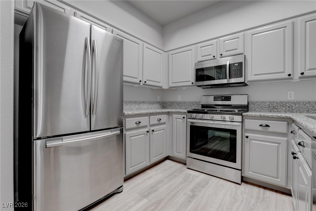 2305 West Horizon Ridge Parkway, Unit 3921 Henderson, NV 89052 - Photo 22 of 31 Kitchen with appliances with stainless steel finishes, white cabinetry, light wood-style flooring, and light stone counters