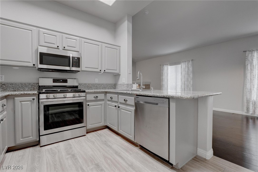 2305 West Horizon Ridge Parkway, Unit 3921 Henderson, NV 89052 - Photo 23 of 31 Kitchen featuring stainless steel appliances, light wood-style flooring, a peninsula, white cabinets, and light stone countertops