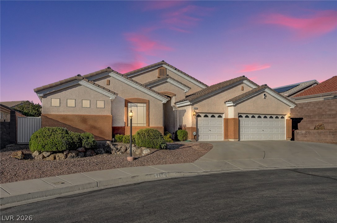 1604 Cattle Ranch Place Henderson, NV 89002 - Photo 1 of 99 A gracefully designed stucco exterior under a vibrant sunset, offering a three-car garage and manicured desert landscaping.