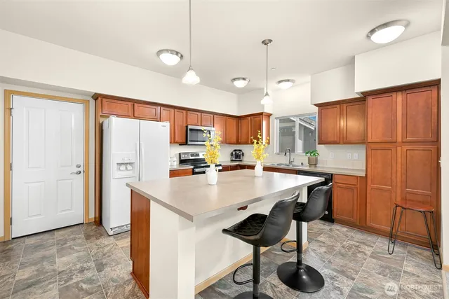 a kitchen with stainless steel appliances granite countertop a refrigerator a sink dishwasher a stove a dining table and chairs with wooden floor