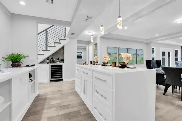 a large white kitchen with stainless steel appliances kitchen island a stove a refrigerator a dining table and chairs with wooden floor