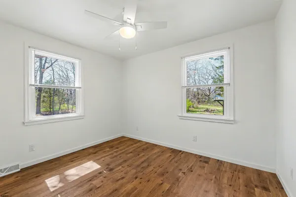 a view of empty room with wooden floor and fan