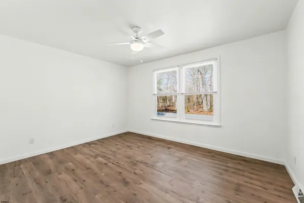 an empty room with wooden floor chandelier fan and windows