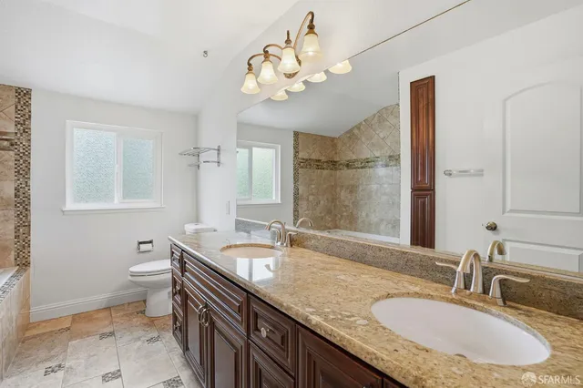 a bathroom with a granite countertop double vanity sink mirror and toilet