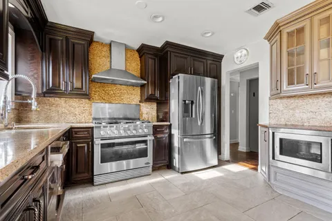 a kitchen with stainless steel appliances granite countertop a refrigerator a stove and a sink with wooden cabinets
