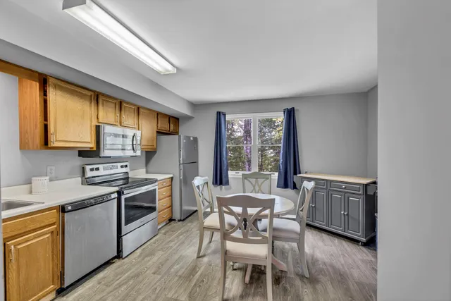 a kitchen with stainless steel appliances granite countertop a stove top oven a sink dishwasher a dining table and chairs with wooden floor