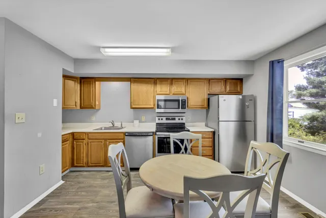 a kitchen with stainless steel appliances a dining table chairs refrigerator and a window