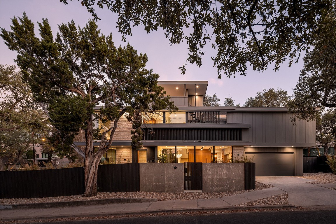 View of front facade featuring concrete driveway, a fenced front yard, a third-story terrace, a garage, and a gate