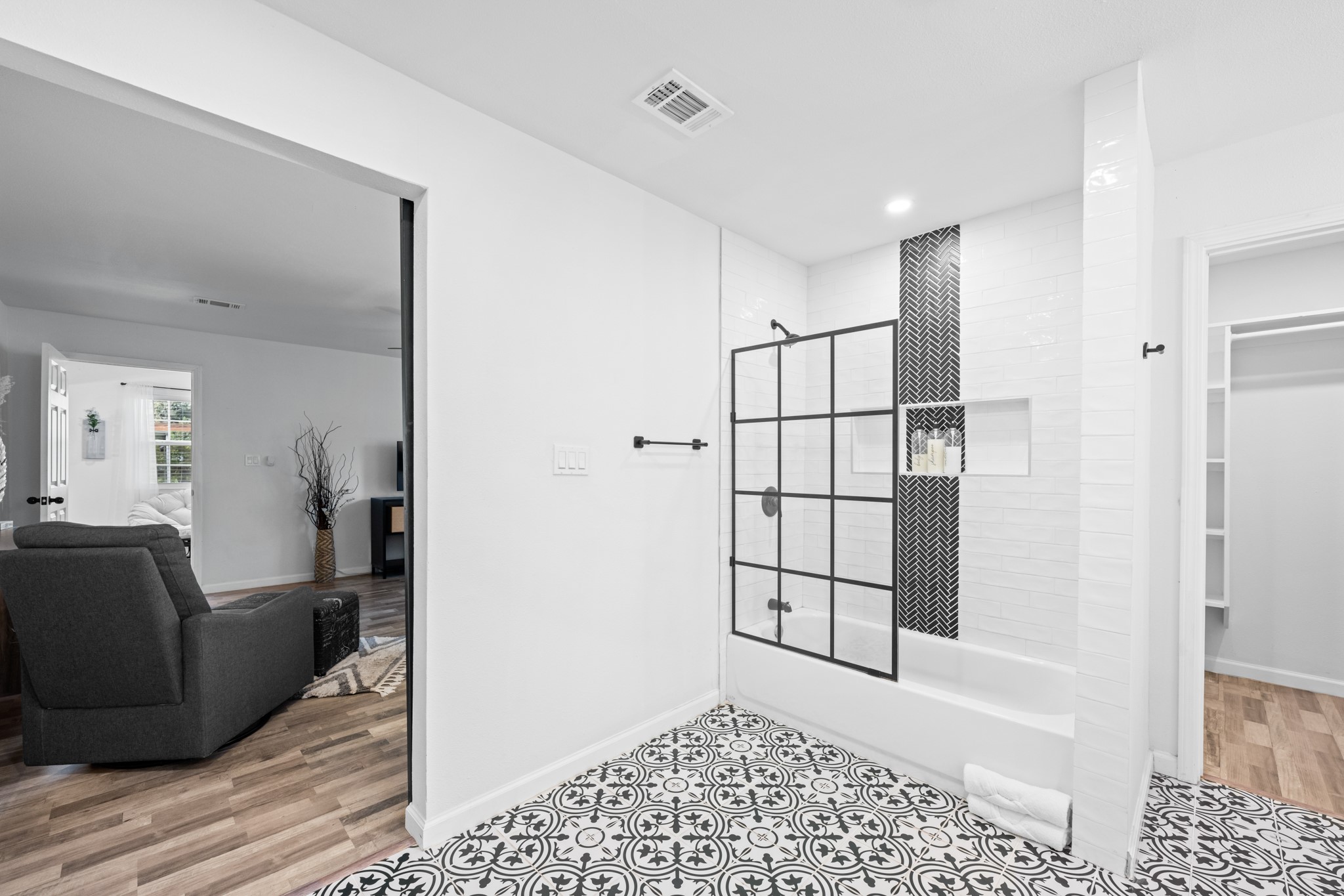 729 Kyle Angleton, TX 77515 - Photo 23 of 36 This photo showcases a modern bathroom with a stylish black and white motif. It features a bathtub with a glass door and decorative tile work. The room connects to the bedroom with wood-look flooring and a cozy atmosphere.