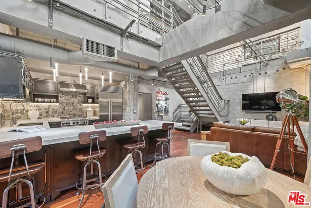 a room with stainless steel appliances kitchen island granite countertop a table chairs and a wooden floors