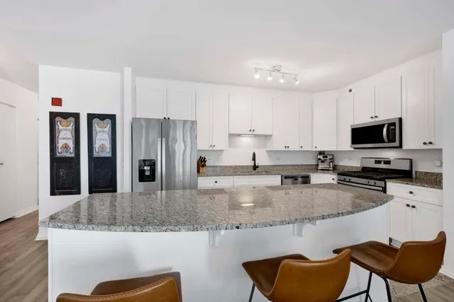 a kitchen with stainless steel appliances granite countertop a stove a sink a refrigerator and white cabinets