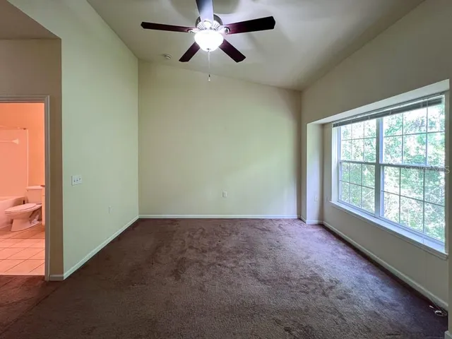 an empty room with chandelier fan and windows