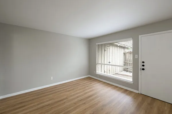 a view of an empty room with wooden floor and a window