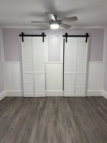 a view of an empty room with wooden floor and a ceiling fan