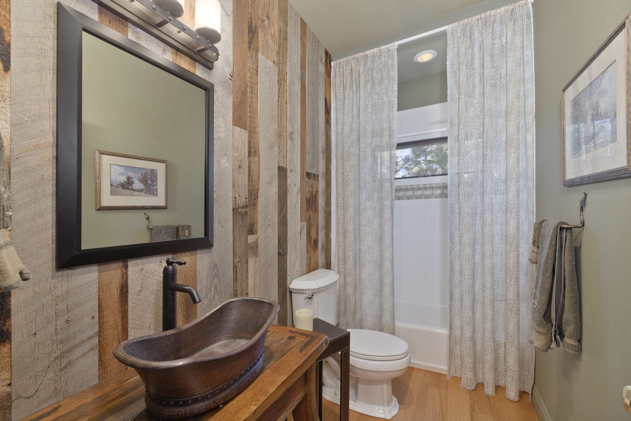 378 Ridge Way Mammoth Lakes, CA 93546 - Photo 33 of 43 Bathroom featuring a vessel sink, wood-finish flooring, a wall-mounted vanity light, a framed mirror, and vertical wood-plank wall accents