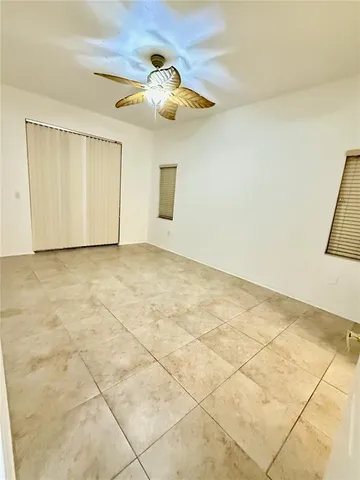 an empty room with a chandelier fan and kitchen view