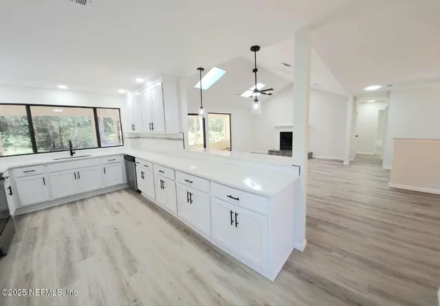 a large white kitchen with a large island wooden floor and stainless steel appliances
