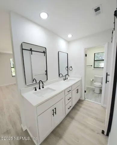 a spacious bathroom with double vanity sink a mirror and a toilet