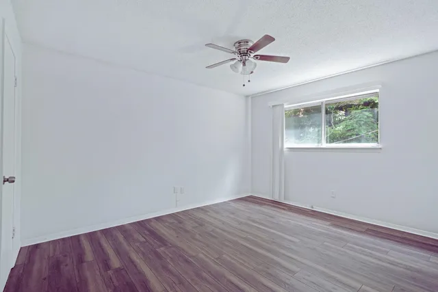 a view of an empty room with wooden floor and a chandelier fan
