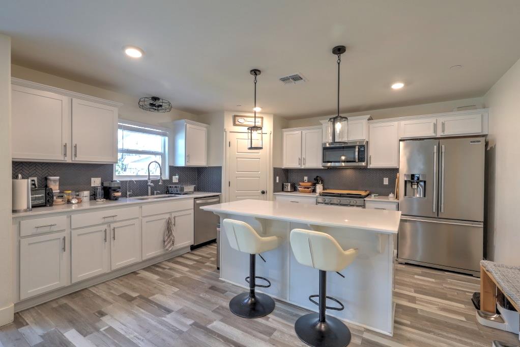 2129 Redding Way Atwater, CA 95301 - Photo 15 of 75 a kitchen with kitchen island a stove a refrigerator and a dining table with wooden floor