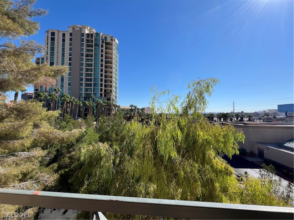 270 East Flamingo Road, Unit 313 Las Vegas, NV 89169 - Photo 19 of 27 City views frame a modern high-rise building with a canopy of green foliage in the foreground.