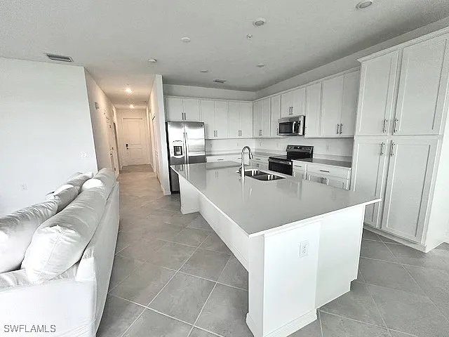a living room with stainless steel appliances furniture a rug and a kitchen view