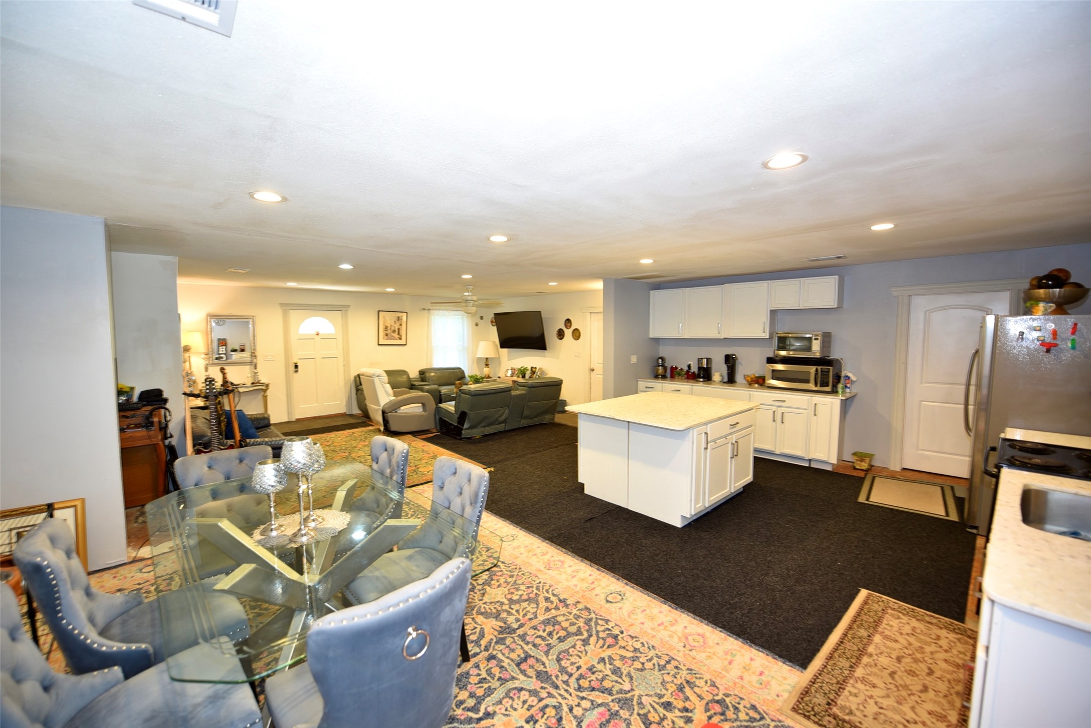 382 Road 5251 Cleveland, TX 77327 - Photo 7 of 22 This open-concept living space features a cozy layout with a kitchen island, stainless steel appliances, and a casual dining area. The room is carpeted with a patterned rug and has recessed lighting, creating a warm and inviting atmosphere.