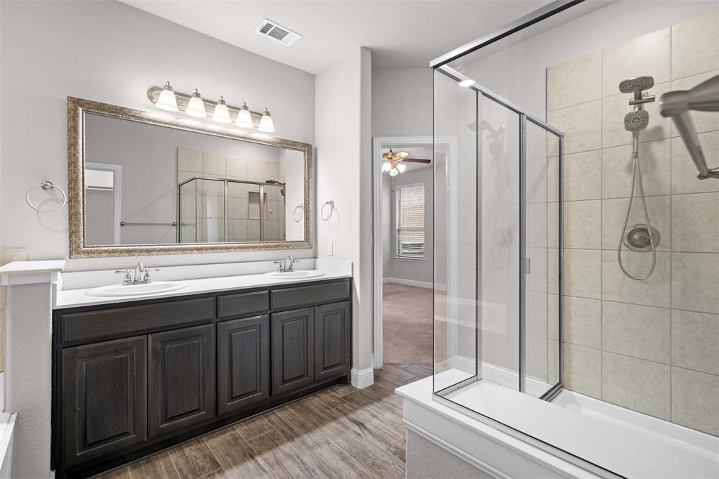 119 Happy Lane Red Oak, TX 75154 - Photo 23 of 37 Bathroom featuring a dual vanity with dark wood-finish cabinetry, a large framed mirror, and a glass-enclosed shower with tiled walls and a handheld shower head