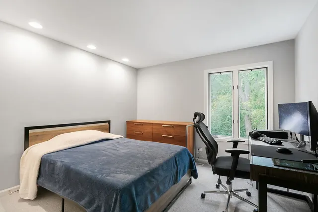 a bedroom with a bed a desk and chair with windows