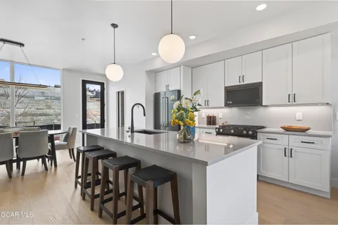 a kitchen with stainless steel appliances granite countertop a stove top oven a refrigerator a sink dishwasher a dining table and chairs with wooden floor