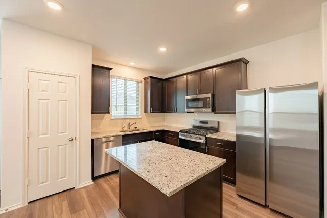 a kitchen with stainless steel appliances granite countertop a stove top oven a sink dishwasher a refrigerator and a oven with wooden floor