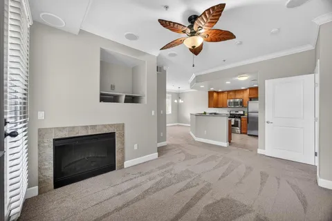 a view of a livingroom with a fireplace a ceiling fan a kitchen refrigerator and a fireplace