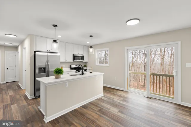 a view of an empty room and kitchen with wooden floor