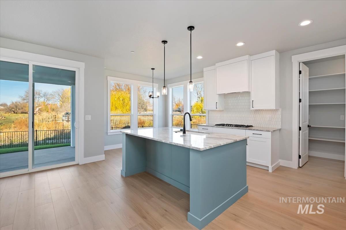 404 Hidden Mill Middleton, ID 83644 - Photo 8 of 41 Kitchen with white cabinets, tasteful backsplash, decorative light fixtures, light stone countertops, and light wood-style flooring