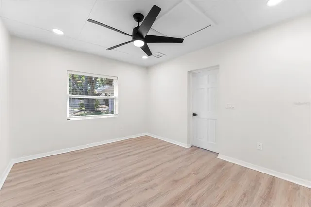 an empty room with wooden floor ceiling fan and windows