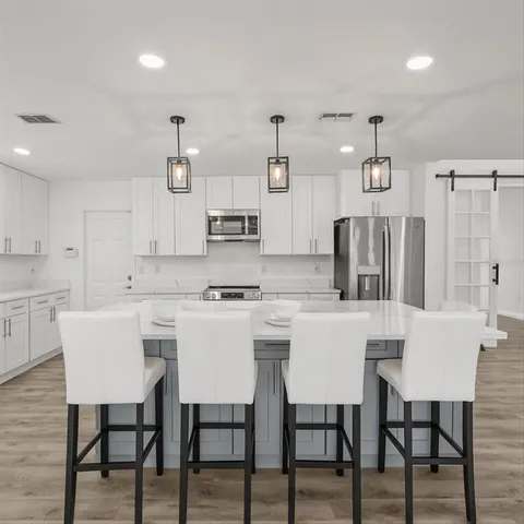 a kitchen with stainless steel appliances granite countertop a dining table chairs refrigerator and sink