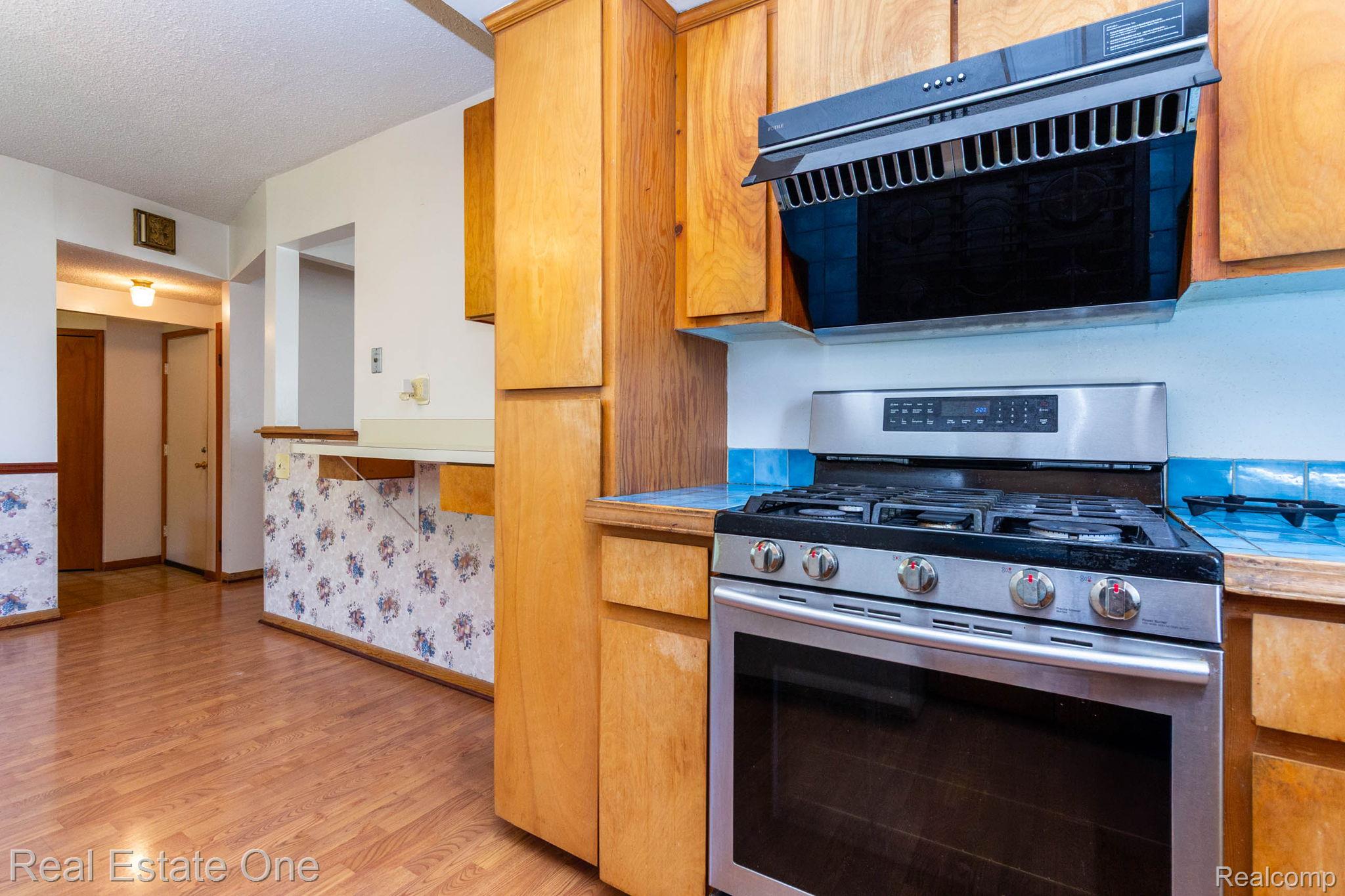 13912 Clinton River Road Sterling Heights, MI 48313 - Photo 10 of 43 Stainless steel range and overhead microwave, wood-finish cabinetry, light countertops, wood-finish flooring, and a breakfast bar