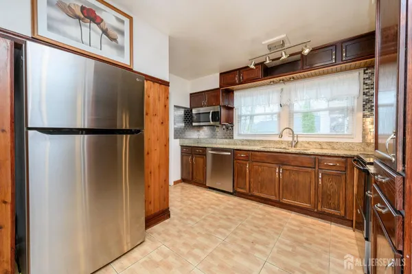 a kitchen with stainless steel appliances granite countertop a refrigerator a sink a stove and a wooden cabinets