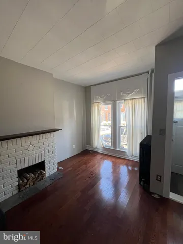 a view of an empty room with wooden floor and a fireplace