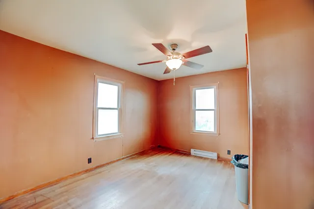 an empty room with wooden floor fan and windows