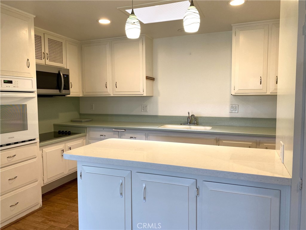 1681 Monterey Road Seal Beach, CA 90740 - Photo 9 of 23 a kitchen with stainless steel appliances granite countertop a sink a stove and white cabinets with wooden floor