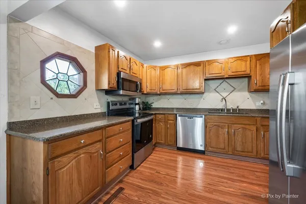 a kitchen with stainless steel appliances granite countertop a sink a stove a refrigerator cabinets and a large window
