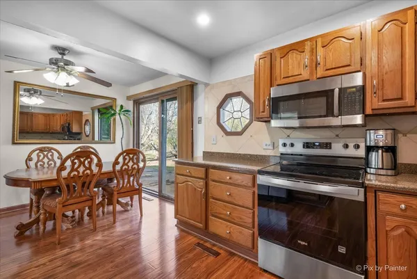 a kitchen with stainless steel appliances granite countertop a stove a microwave a dining table and chairs with wooden floor