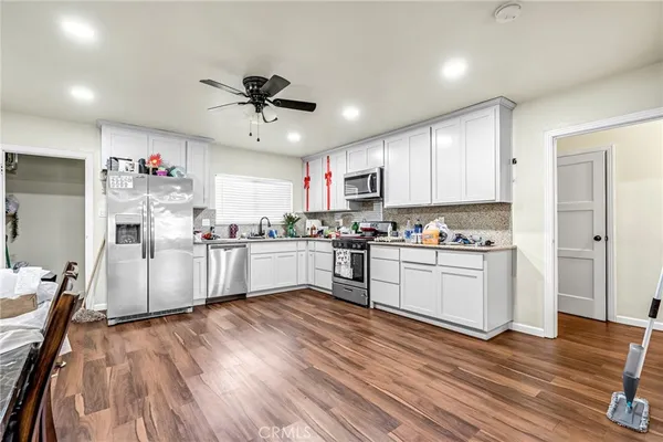 a kitchen with granite countertop a refrigerator oven a sink dishwasher and white cabinets with wooden floor