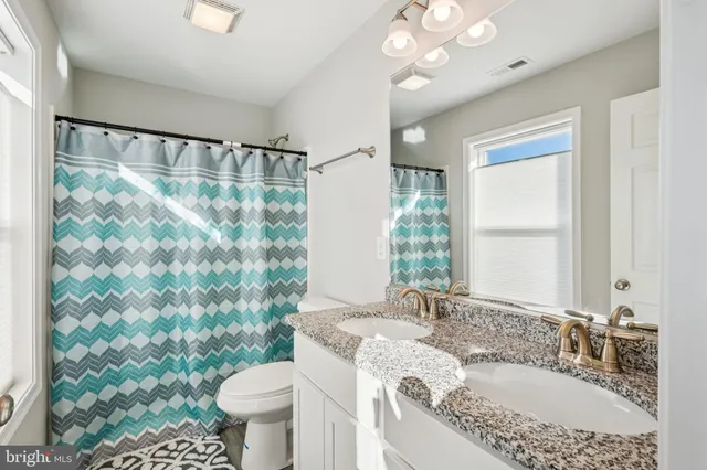 a bathroom with a granite countertop sink a toilet a mirror and shower curtain