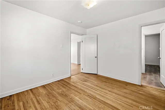 an empty room with wooden floor and way to kitchen