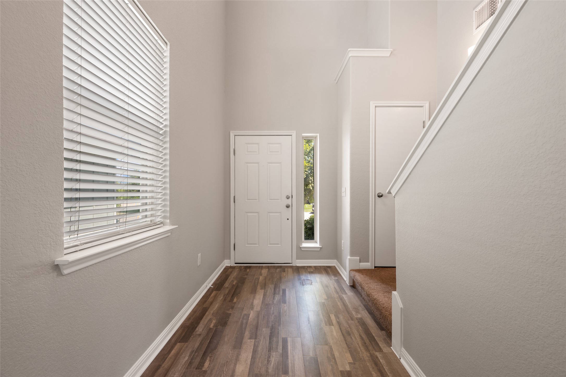 A welcoming entryway features rich wood flooring, leading to a tall ceiling with a clear sightline up the staircase.